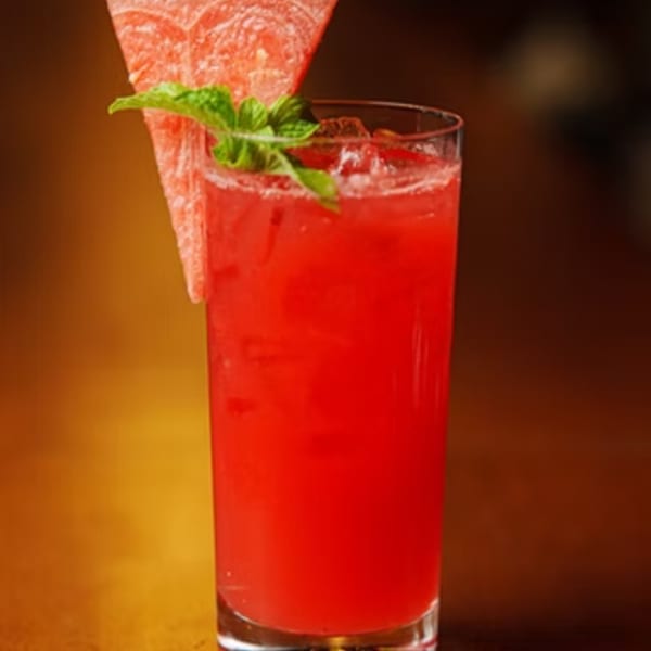 Red watermelon drink with ice, garnished with a watermelon slice and mint leaves.