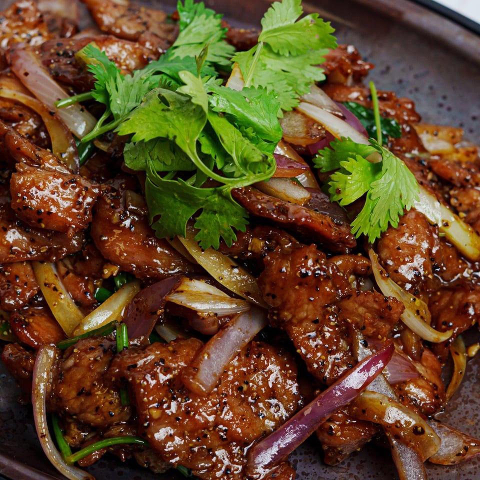 Fulin's Asian Cuisine's Chinese black pepper beef with onions and cilantro on a dark plate.