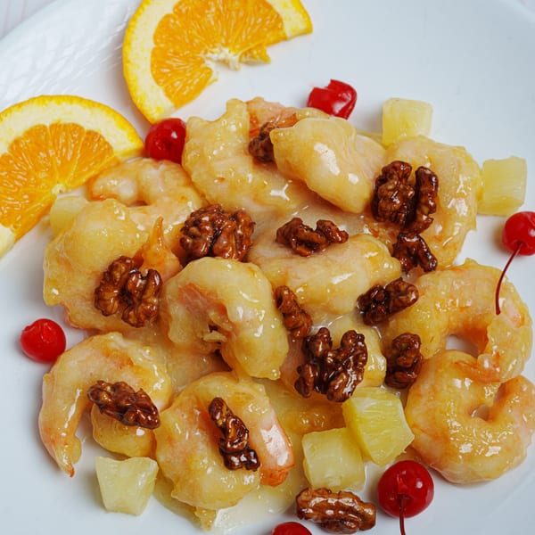 Honey walnut shrimp with pineapple, cherries, and orange slices on a white plate.