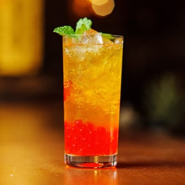 A tall glass of Fulin's Asian Cuisine's vibrant yellow and red drink with ice and mint.