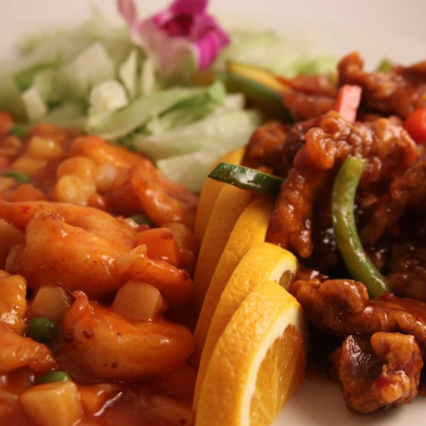 Sweet and sour shrimp and chicken with orange slices and lettuce on a white plate.